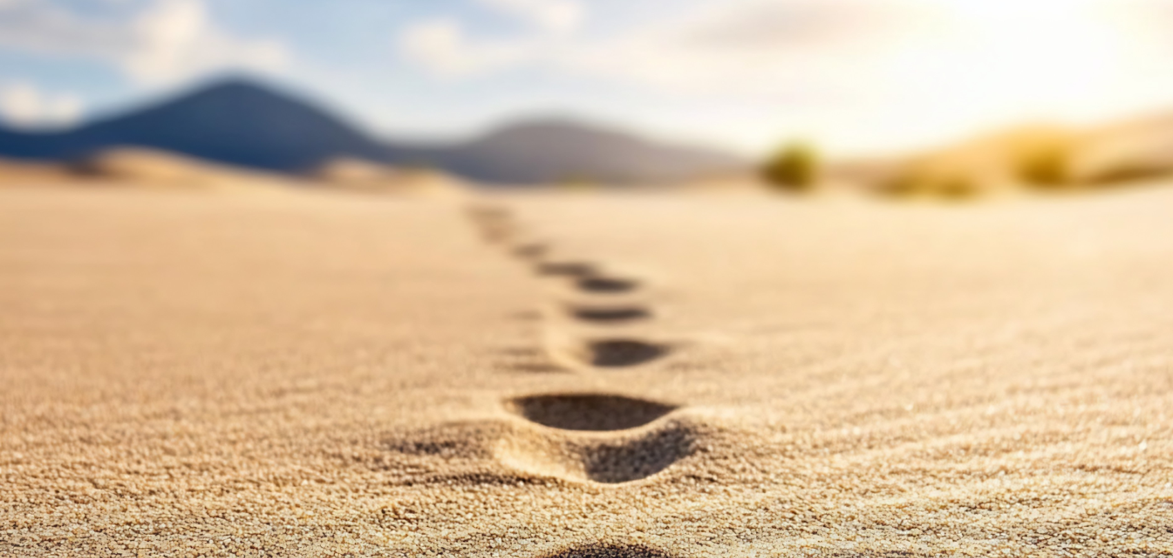 Footprints leading across sand towards distant hills